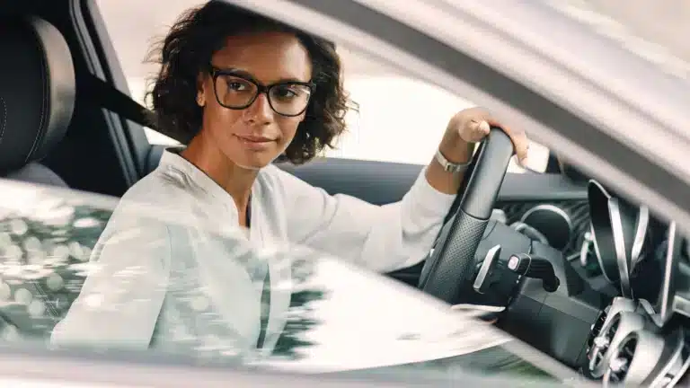 A woman wearing glasses is driving a car for the Last Mile.