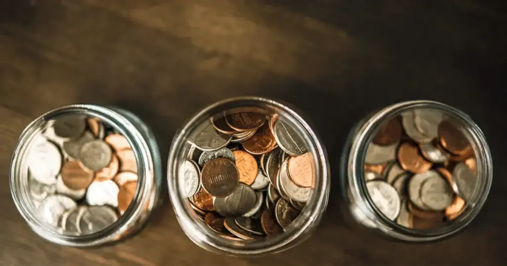 Three jars filled with coins on a wooden table.