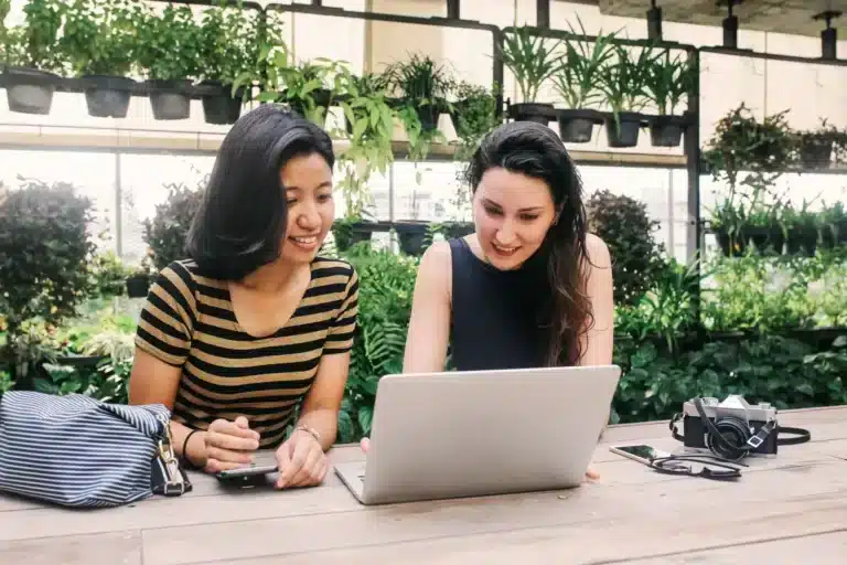 Two asian women sitting at a table looking at a laptop.