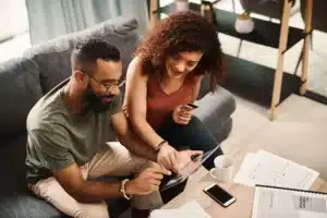 A man and woman sitting on a couch looking at a tablet.