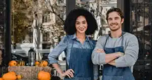 A couple in aprons standing in front of a pumpkin stand.
