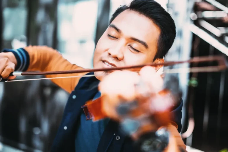 A young man playing the violin in front of a building.