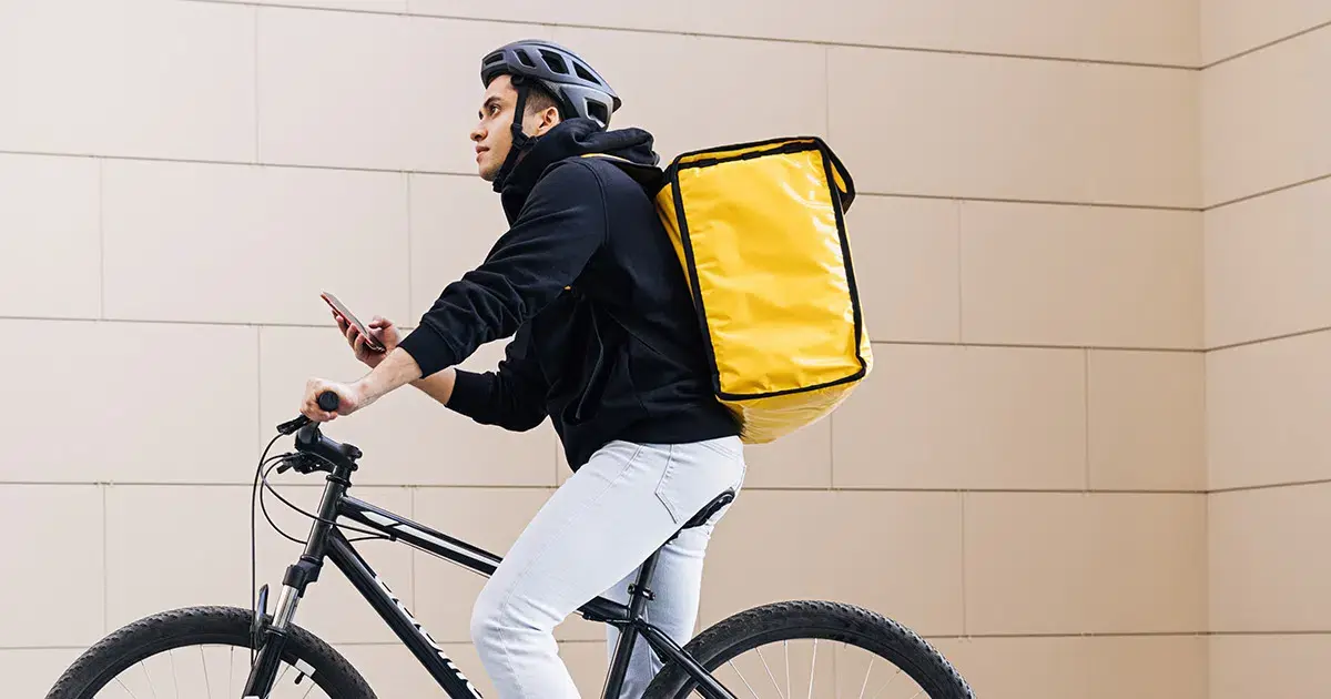 A man riding a bicycle with a yellow bag on his back.