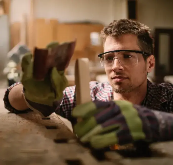 A man wearing glasses is working on a piece of wood.