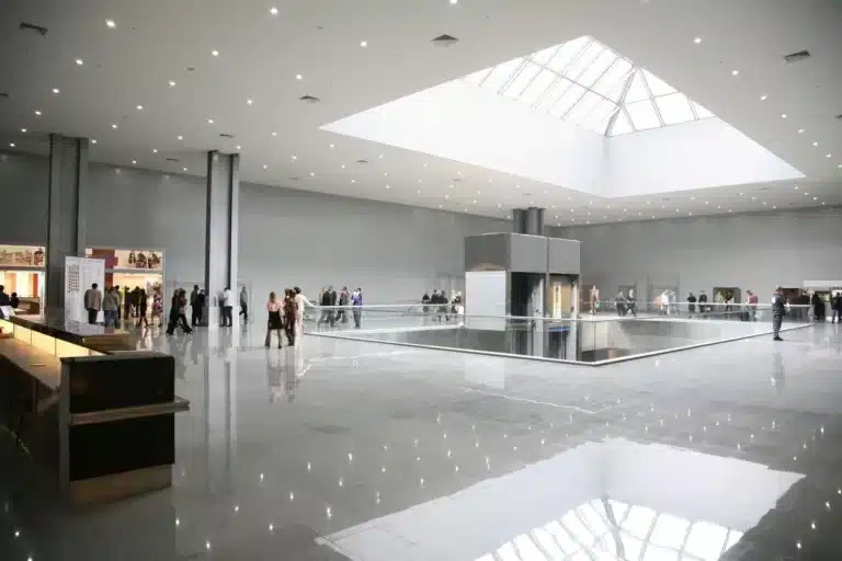 The interior of a large glass building with people walking around.
