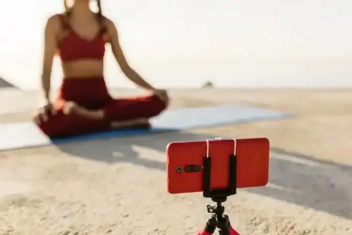 A woman is doing yoga on the beach with her phone.