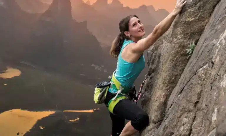 A woman climbs up a cliff at sunset.