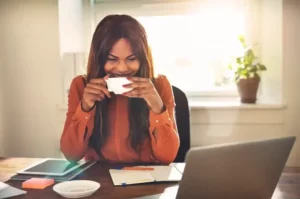 A woman drinking a cup of coffee while working at her desk.