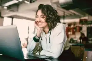 A woman is smiling while using a laptop.
