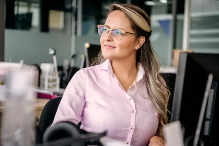 A woman wearing glasses is sitting at a desk in an office.