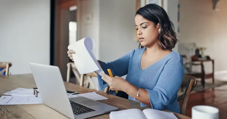 A woman sitting at a table with a laptop and papers.