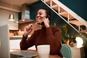 A woman is talking on the phone while sitting at a table with a laptop.