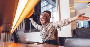 A muslim woman with her arms outstretched in front of a laptop.