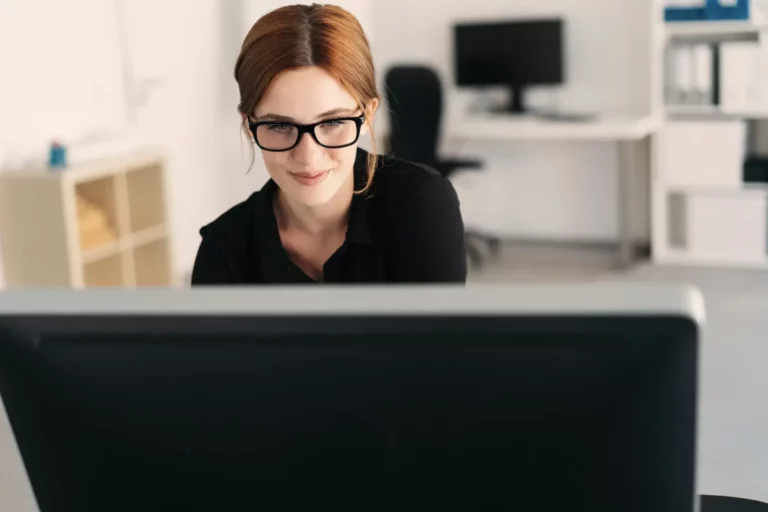 A woman wearing glasses is sitting in front of a computer.