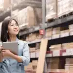 Asian woman holding a tablet in a warehouse.