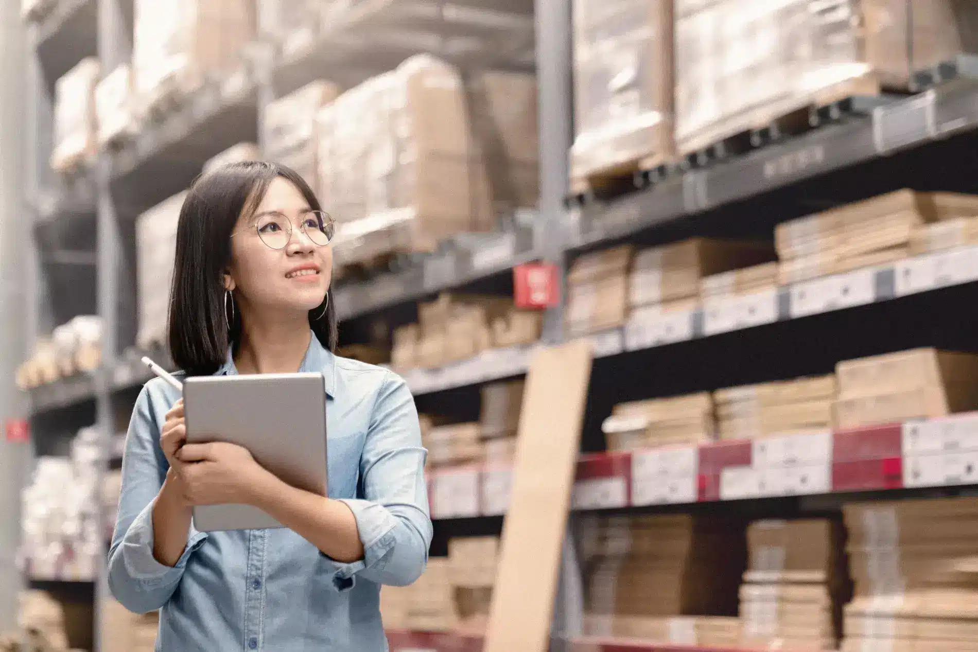 Asian woman holding a tablet in a warehouse.