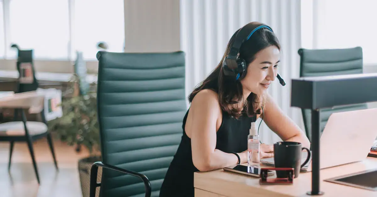 A woman wearing a headset at a desk in an office.