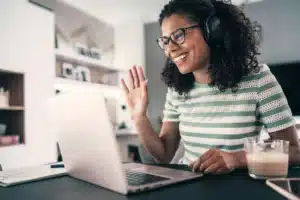 A woman wearing headphones and waving at a laptop.