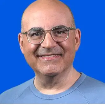 A bald man with glasses smiling in front of a blue background.