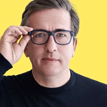 A man in glasses is posing against a yellow background.