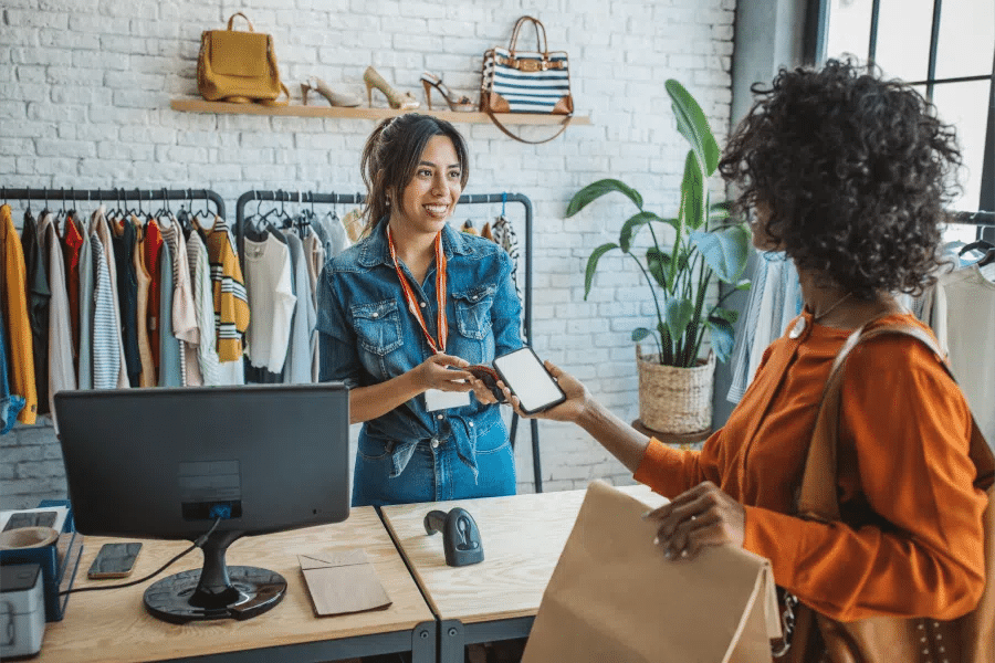 A woman is handing a woman a shopping bag in a clothing store.