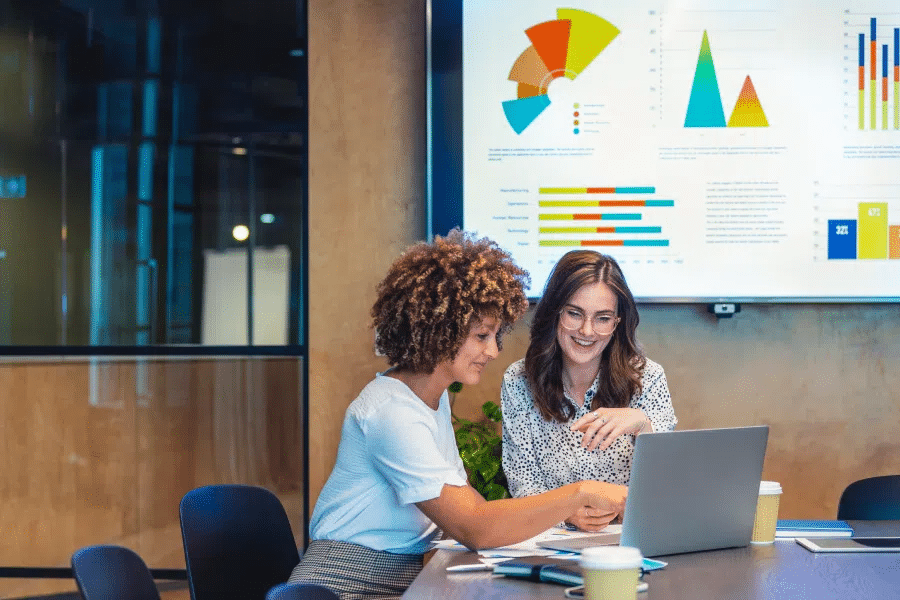 Two women working on a laptop in a conference room.