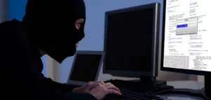A man in a black mask sitting at a computer.