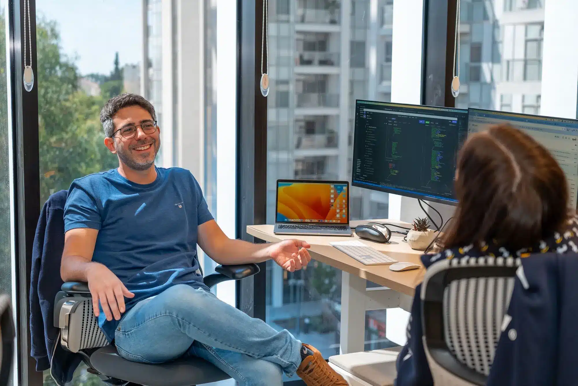 A man and woman sitting in front of two computer monitors.