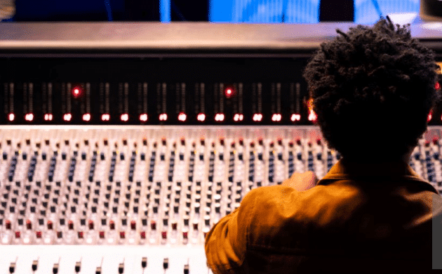 A person with curly hair creates perfect synergy as they operate a large audio mixing console, blending the sounds harmoniously in their cozy home studio.