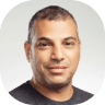 Portrait of a man with short hair and a neutral expression, wearing a dark T-shirt about to capture the essence of synergy, against a light gray background.