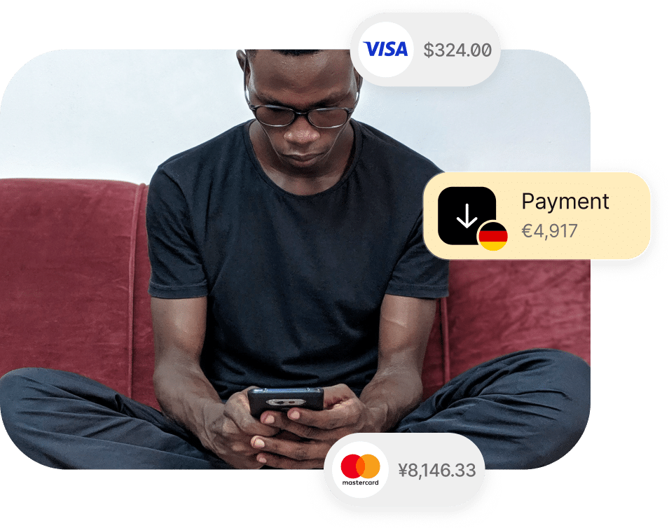 A person in a black shirt and glasses is using a smartphone while sitting cross-legged on a red couch. Payment icons with amounts in different currencies appear around them.