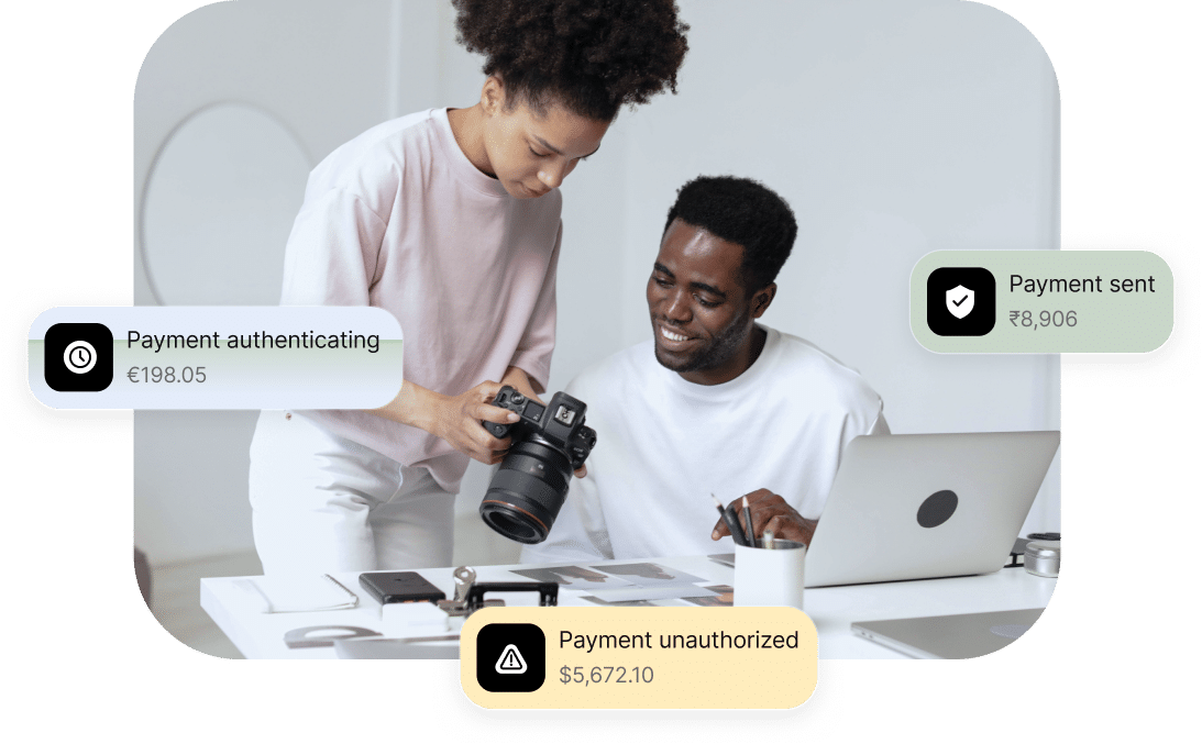 Two people work together, one holding a camera, at a desk with a laptop, smartphone, and documents. Surrounding messages display payment statuses: "Payment authenticating," "Payment unauthorized," and "Payment sent.