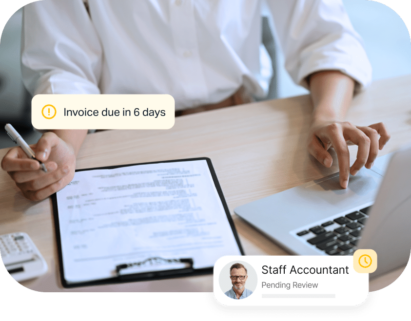 A person reviews a clipboard document and types on a laptop. Notifications about an invoice due in 6 days and a pending review from a staff accountant are visible.