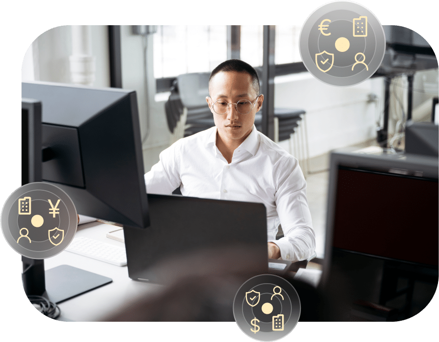 A man in a white shirt works at a desk with multiple computer monitors. Three floating icons, depicting financial symbols, surround him.