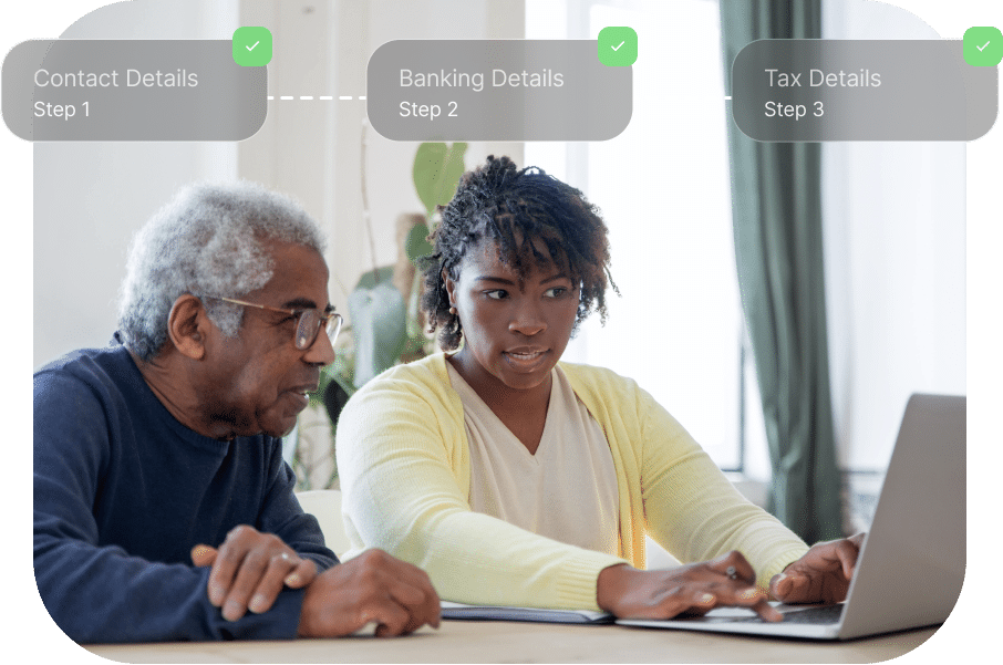 Two people sitting at a table using a laptop, focusing on a webpage showing a three-step process labeled as Contact Details, Banking Details, and Tax Details.