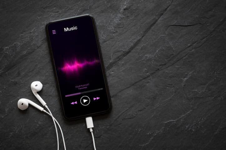 A smartphone playing music with earbuds attached rests on a dark slate surface, illustrating the seamless blend of technology and creativity that drives modern industries.