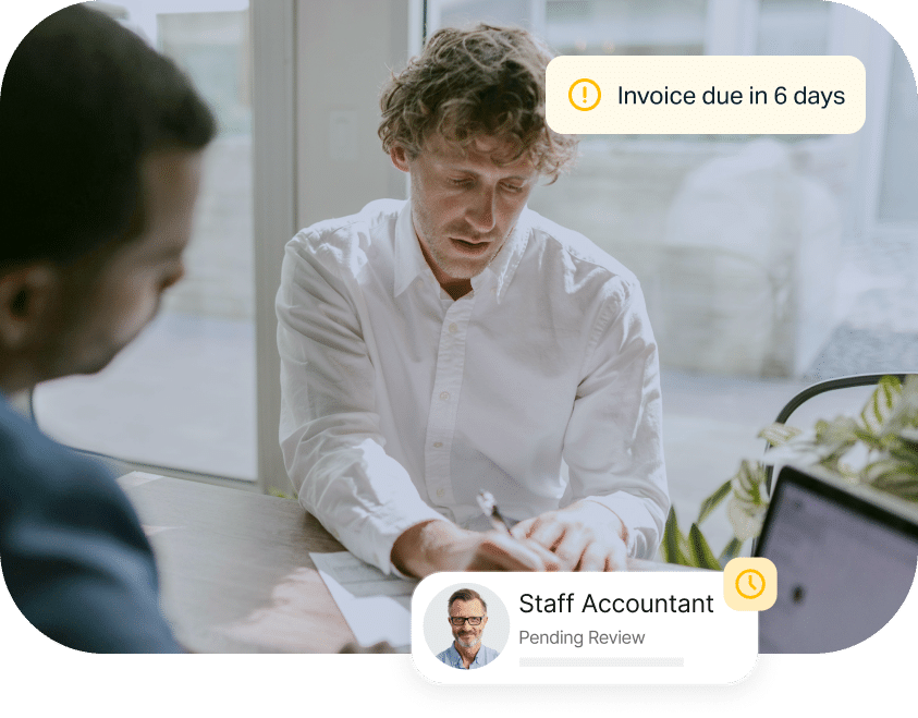 Two men sit at a table, one writing on paper. Overlaid text reads "Invoice due in 6 days" and "Staff Accountant Pending Review". Nearby is an open laptop.