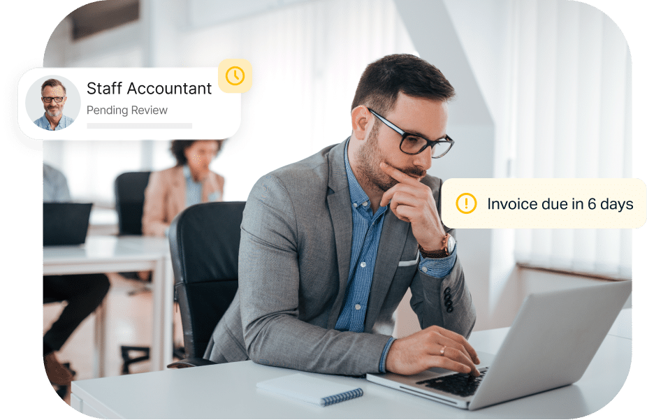 A man in an office works on a laptop. Two notifications appear: "Staff Accountant Pending Review" and "Invoice due in 6 days." Other people work in the background.