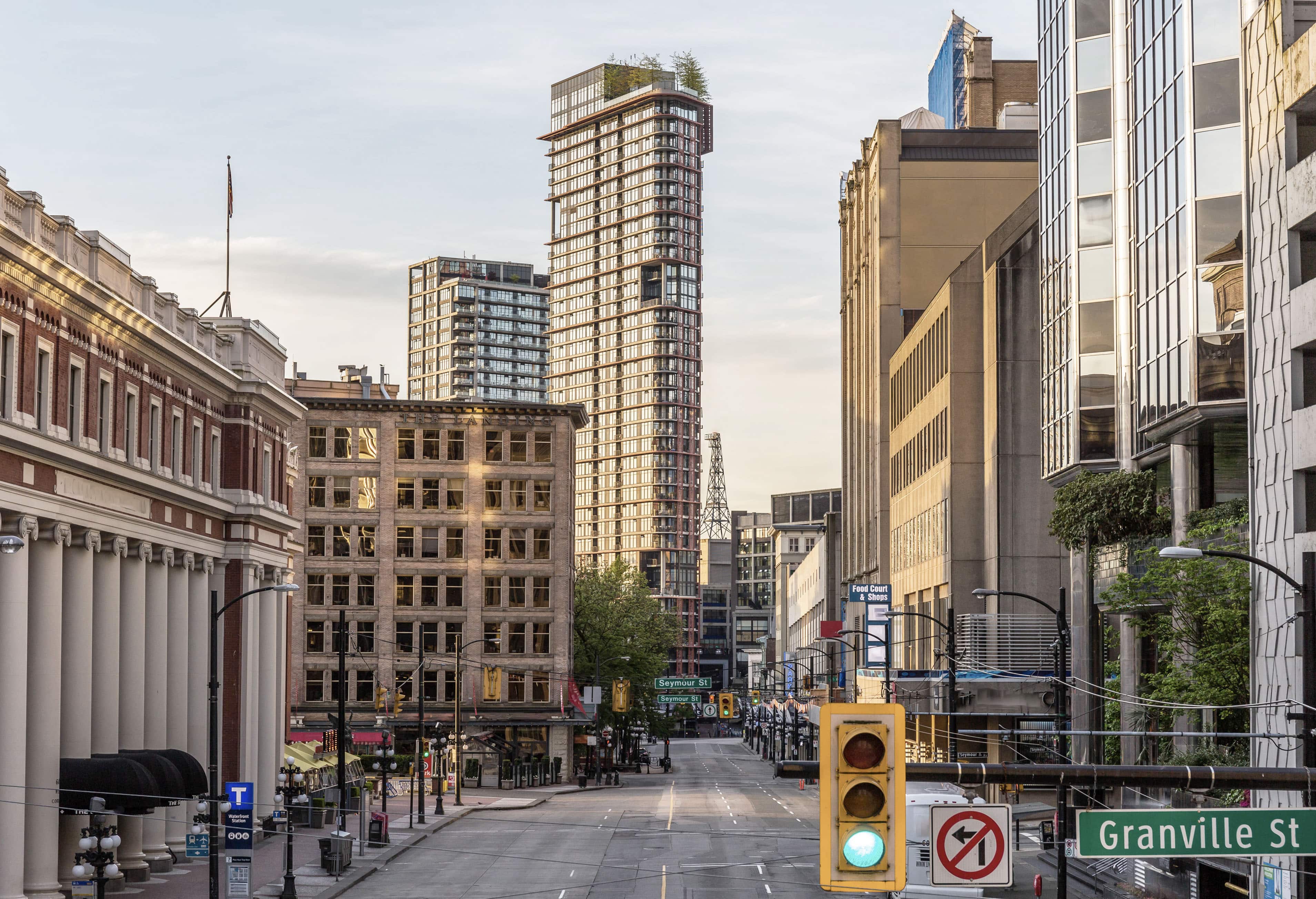 A city street scene with tall buildings lining both sides. A traffic light is visible in the foreground near a Granville St sign.