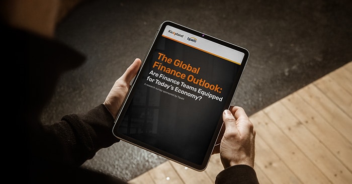 A person holds a tablet displaying a report titled "The Global Finance Outlook: Are Finance Teams Equipped for Today’s Economy?.