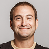 A man with short brown hair and a slight smile is facing the camera against a plain light gray background.