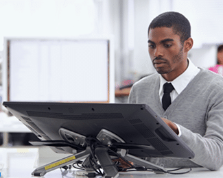 A man in a grey sweater and tie working at a computer in an office.