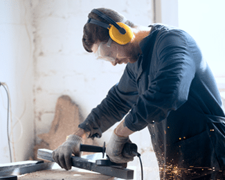 A worker wearing safety goggles and ear protection uses an angle grinder on a metal bar, producing sparks.