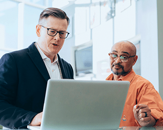 Two men in business attire look at a laptop screen together.